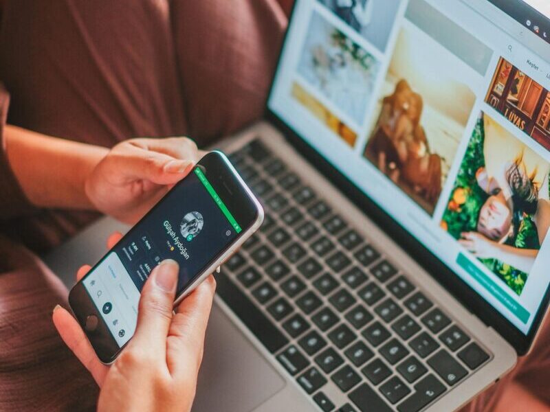 Person using a laptop and smartphone simultaneously indoors, showcasing multitasking.