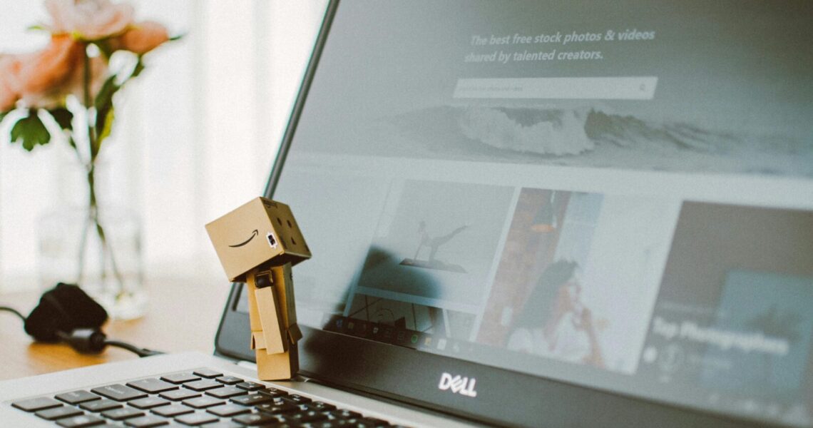 A small toy figure stands on a laptop keyboard with flowers in the background.