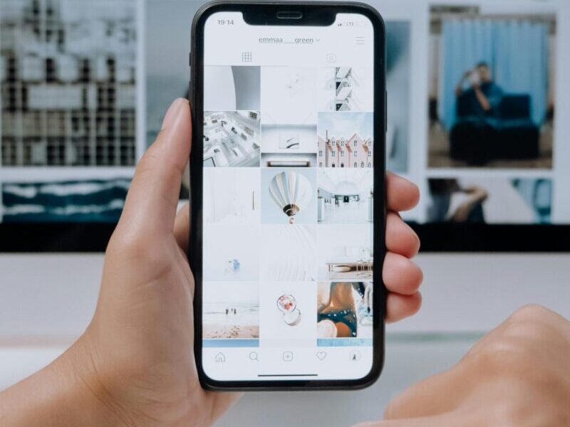 Person using smartphone to browse photos, office desktop setup.